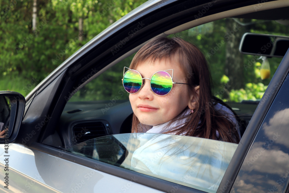 The concept of car travel with children. Eight-year-old girl wearing sunglasses in a car in nature on a sunny day, close-up