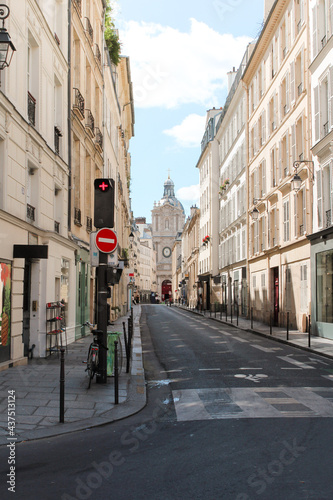 Fototapeta Naklejka Na Ścianę i Meble -  A narrow street in Paris, France, that ends in a small church on a sunny summer day, with shops, houses, people, windows with hanging flowers, and everything in bright colors.