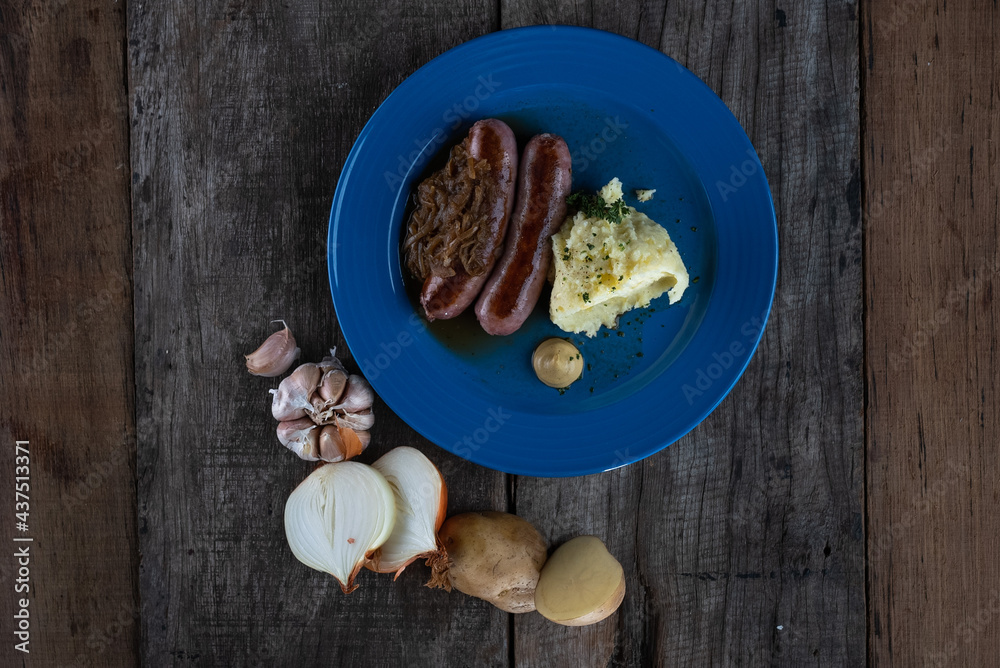Top view of pork sausages in onion gravy sauce served with mashed potatoes isolated on wooden table Top view of pork sausages in onion gravy sauce served with mashed potatoes isolated on wooden table