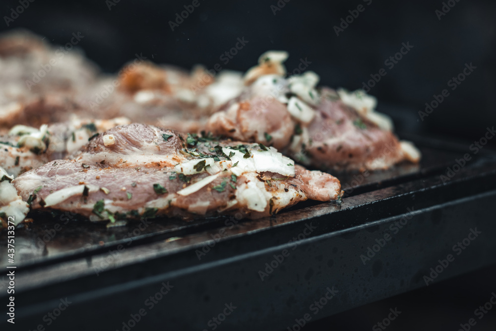 Wonderful detail of grilling pork neck meat on a granite stone laid on the heat of the fire. Meat sprinkled with salt, basil, rubbed with oil. Barbecue season has begun