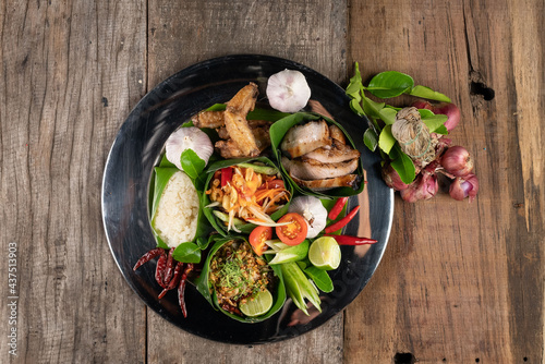 Set of Thai style food with rice, minced pork, papaya salad, pork steak and spare ribs served in banana leaves isolated on wooden table