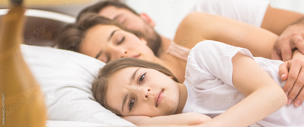 The girl lay near the sleeping parents on the bed The girl lay near the sleeping parents on the bed