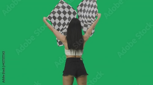 Rear view of sexy brunette in short shorts waving black and white checkered racing flags. Young woman posing against background of green screen in studio close up. Slow motion ready, 4K at 59.94fps. photo