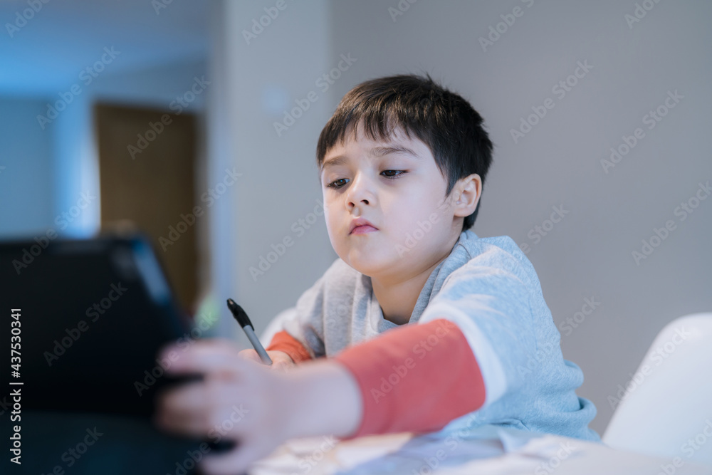 Authentic Portrait of preschool kid using tablet for his homework, New normal life child boy use touch pad for home learning, E-learning or Homeschooling education concept Authentic Portrait of preschool kid using tablet for his homework, New normal life child boy use touch pad for home learning, E-learning or Homeschooling education concept