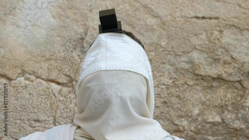 A Jewish man is praying in front of the Wailing Wall, the camera is behind him, focused on the Jewish praying shawl and the Tefillin. a 4K 29.97 fps clip, old city of Jerusalem, Israel. photo