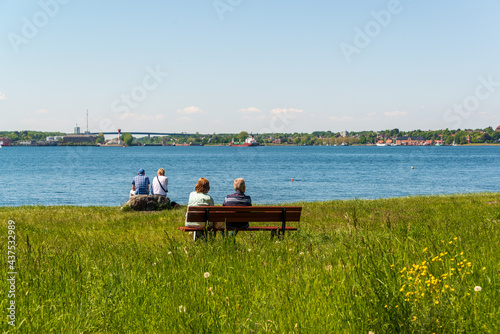 Am Strand von Kitzeberg zwei Sitzbänke mit älteren Personen und Blick über die Kieler Förde auf die Einfahrt zum Kiel Canal