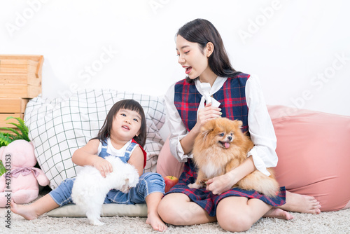 A young Japanese woman and a girl embracing Maltese and Pomeranian dogs in the living room.