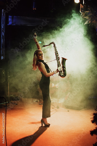 Canvas Print Beautiful young blond woman playing saxophone on stage of a night jazz club; roa