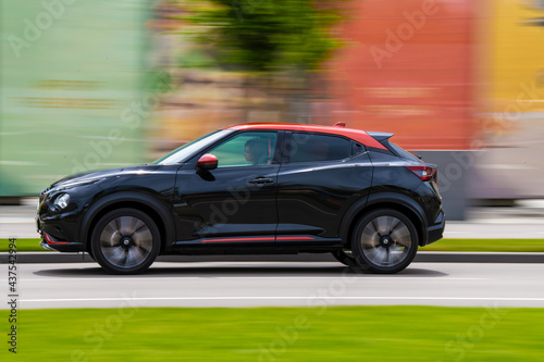 Side view of high speed luxury modern electric SUV car driving in the city streets. Blurred colorful background.