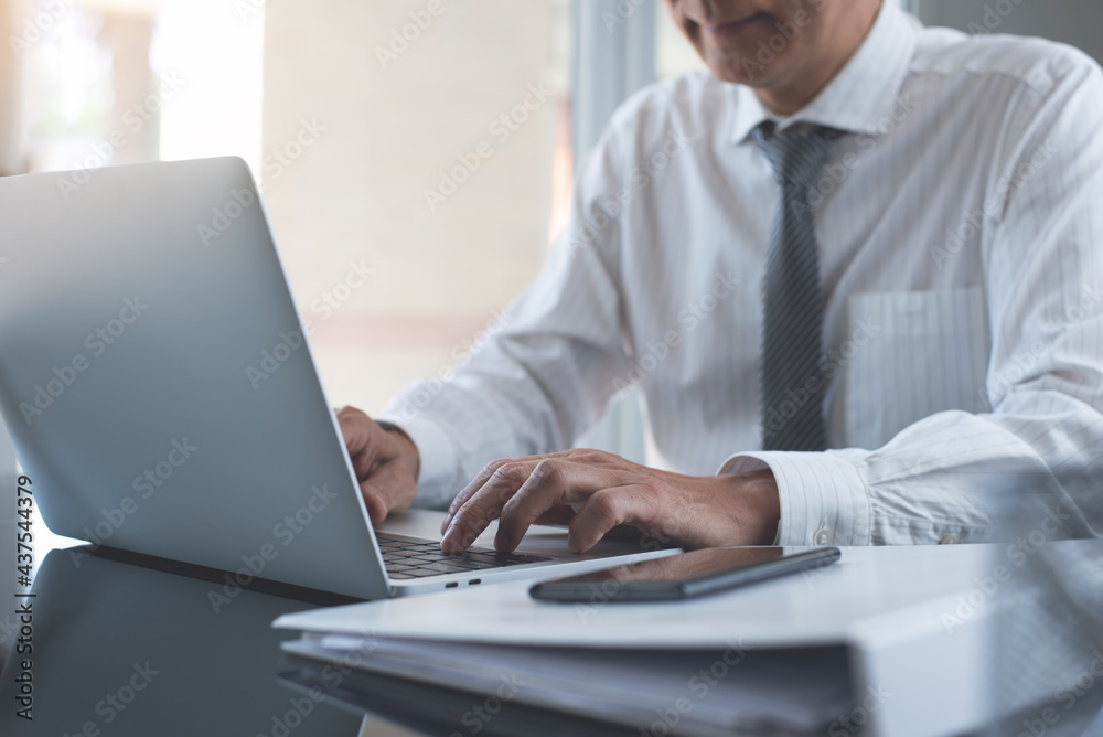 Businessman working on laptop computer with business document on table in modern office