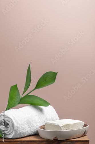 Spa concept: towel, organic soap and green branch are on wooden shelf against light pink background.