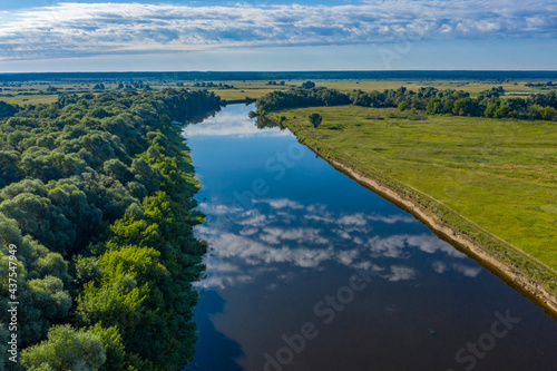 Aerial view of a beautiful summer landscape over river while dawn. Top view over river with a smooth water surface reflecting blue sky and clouds.
