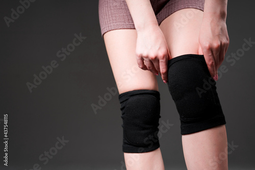 Photo of female hands. The girl pulls a black knee pad on her leg. Isolated on dark background