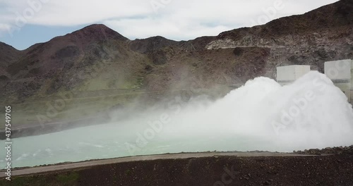 Dam with large discharge pressure of the water. Water dam. Shooting with the drone. Huge water pressure. Big fountain. Around the fountain grows grass, trees, running river. Summer nature. Small rocks photo