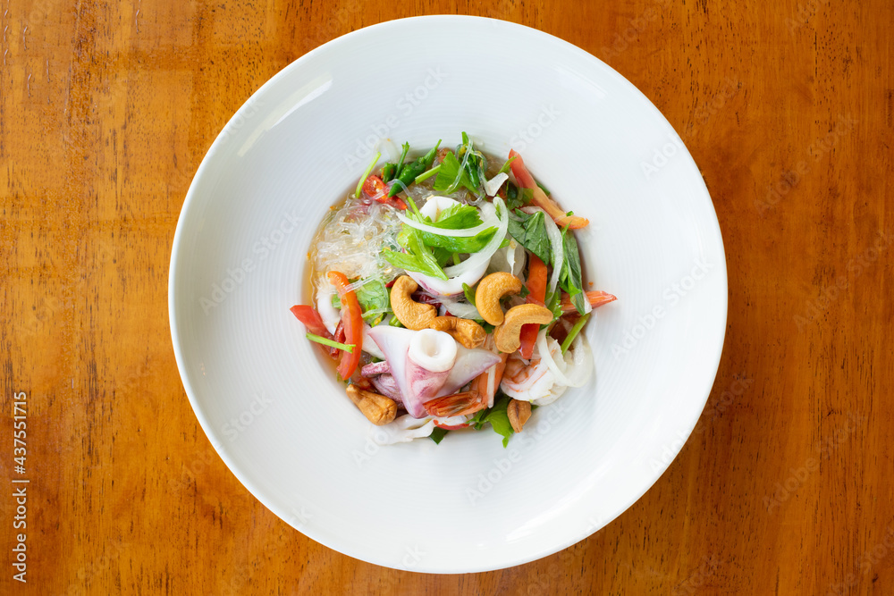 Vermicelli spicy salad with seafood and cashew in white dish on wooden table. Vermicelli spicy salad with seafood and cashew in white dish on wooden table.
