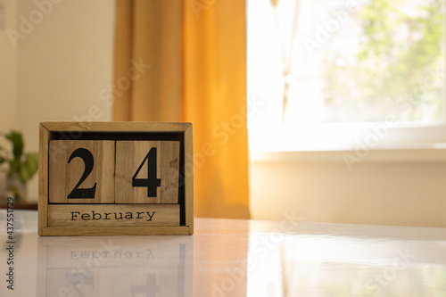 Wooden blocks of the calendar represents the date 24 and the month of February on the background of a window, curtain and a plant