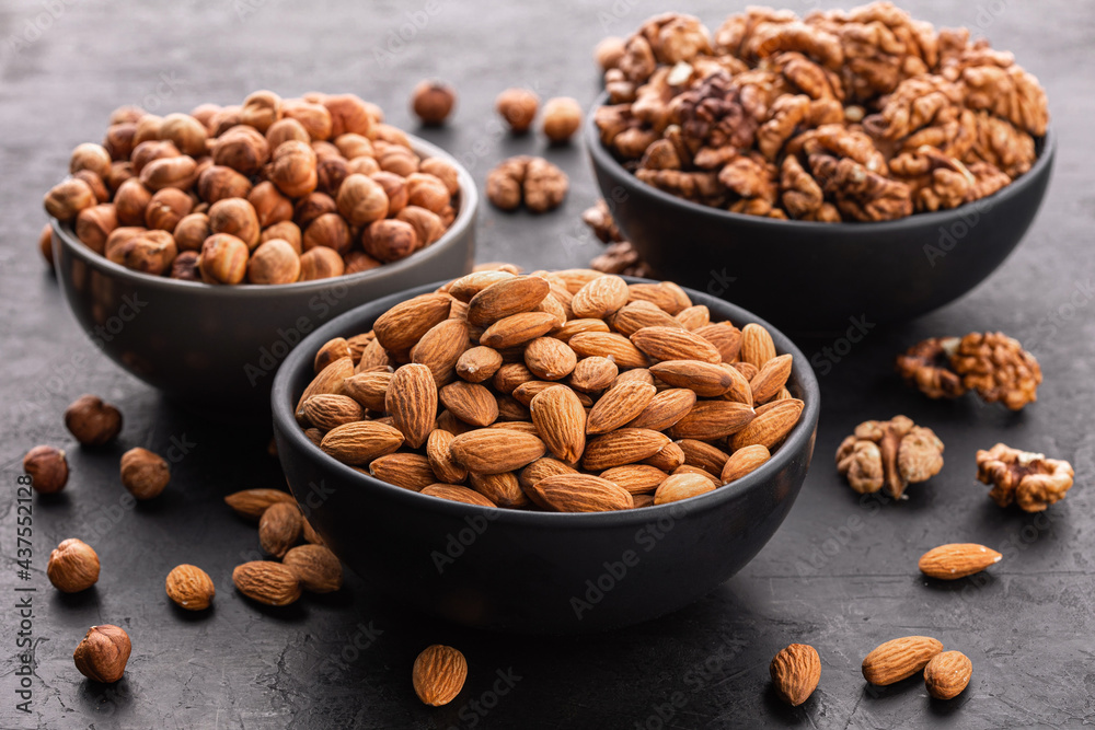 Assorted nuts. Close-up, peeled walnuts, almonds and hazelnuts in bowls on a black wooden background, side view. Assorted nuts. Close-up, peeled walnuts, almonds and hazelnuts in bowls on a black wooden background, side view.