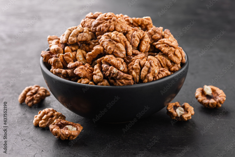 Peeled walnut in a bowl and a few nuts scattered around on a black textured background, side view. Peeled walnut in a bowl and a few nuts scattered around on a black textured background, side view.