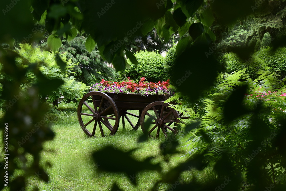 view of the park decoration in the form of a cart with flowers through the foliage
