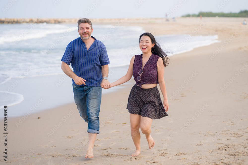 young beautiful and happy mixed ethnicity couple of Asian woman and Caucasian man relaxed and cheerful walking playful on beach enjoying love and romantic holidays young beautiful and happy mixed ethnicity couple of Asian woman and Caucasian man relaxed and cheerful walking playful on beach enjoying love and romantic holidays