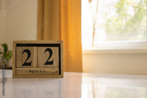 Wooden blocks of the calendar represents the date 22 and the month of April on the background of a window, curtain and a plant.