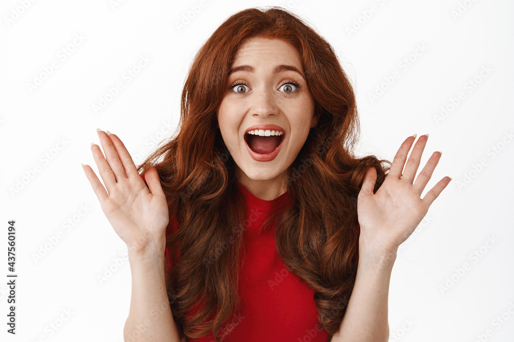 Portrait of amazed surprised redhead girl, staring astonished at camera, being fascinated by something awesome and super cool, standing against white background Portrait of amazed surprised redhead girl, staring astonished at camera, being fascinated by something awesome and super cool, standing against white background