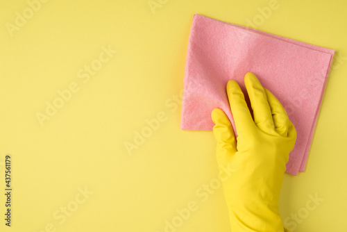 Top view photo of hand in yellow rubber glove using viscose napkin on isolated yellow background with copyspace