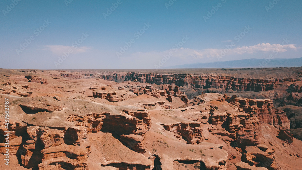 Fototapeta premium Grand canyon Charyn. Rocks from sedimentary rocks. Huge cracks in the rocks. The ground is red-orange. Top view from a drone. There is a road in the center. Layers of earth in different colors.