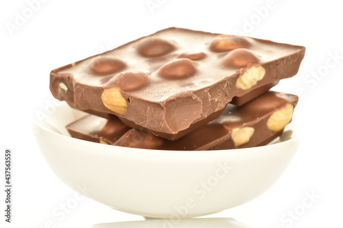 Several slices of dark chocolate with nuts on a white ceramic saucer, close-up, isolated on white.