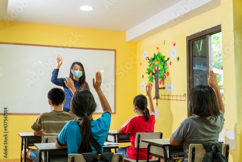 Asian teacher with face mask welcoming children back at school after lockdown..