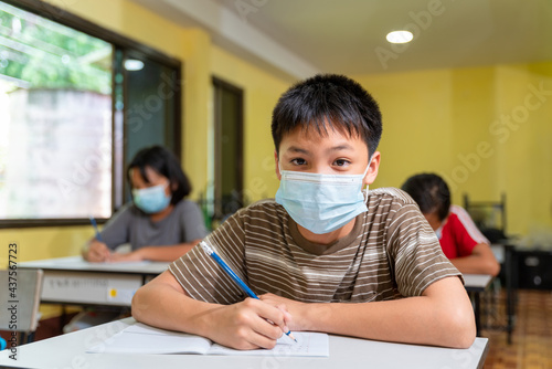 Asian boy in classroom with face mask back at school after covid-19 quarantine and lockdown.