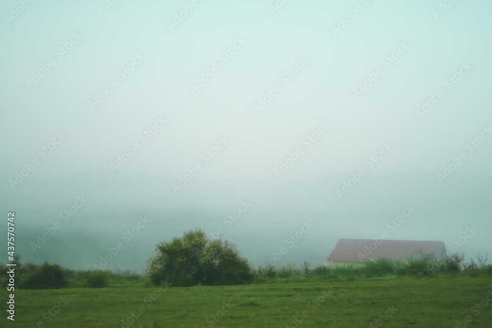 Morning landscape with wooden cottege house for tourists in the Carpathian mountains with the background of mountains covered by thick fog.
