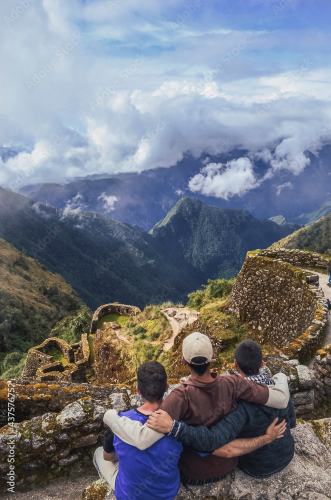 High angle view of three backpacker male friends hugging each other on Phuyupatamarca ruins with the huge valley in front of them. Inca trail to Machu Picchu in Peru. South America