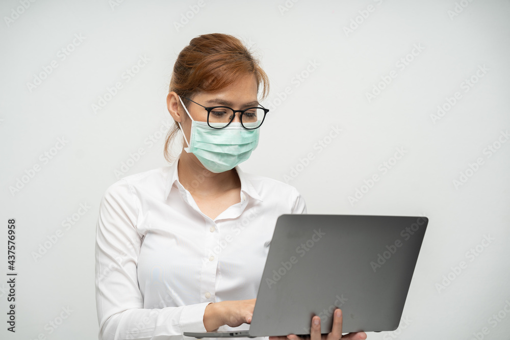 Pretty office worker wearing a mask using a laptop to work.
