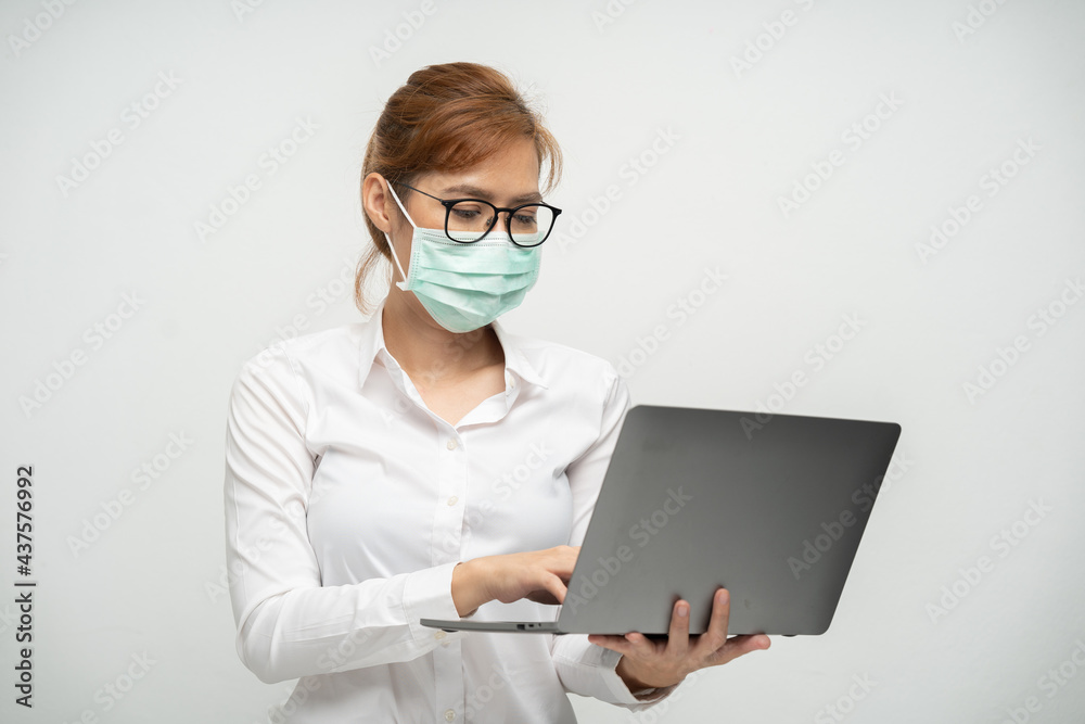Pretty office worker wearing a mask using a laptop to work.