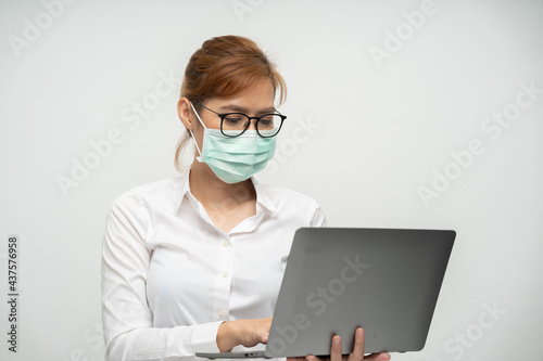 Pretty office worker wearing a mask using a laptop to work.