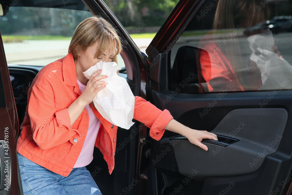 Woman with paper bag suffering from nausea in car