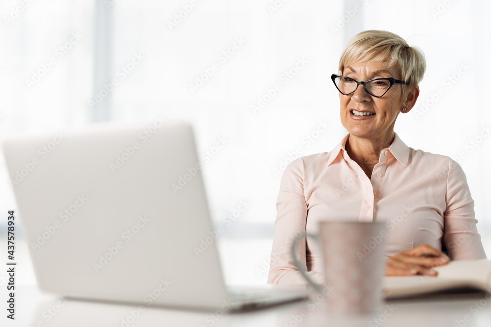Smiling mature businesswoman working on laptop and taking notes in the office Smiling mature businesswoman working on laptop and taking notes in the office