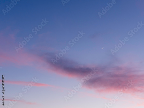 Fototapeta Naklejka Na Ścianę i Meble -  Beautiful sunset with pink clouds on clear blue sky with  sickle of the waxing moon. Colorful panorama of heavens. Peaceful atmosphere of evening. Dusk time of a day.