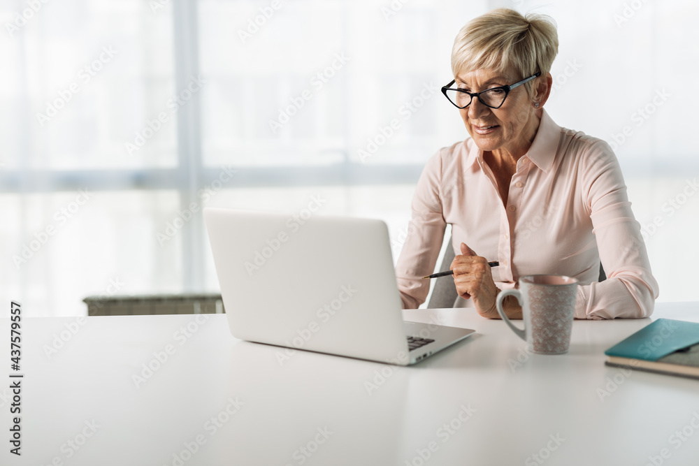 Mature businesswoman reading an e-mail on her computer in the office Mature businesswoman reading an e-mail on her computer in the office
