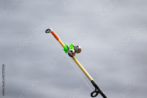The bells of the allure are attached to the end of the fishing spinning abandoned in the water and standing with a stretched fishing line. Bottom rod and fishing accessories on a blury background.