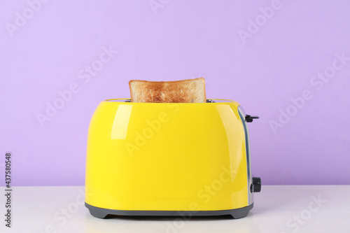 Modern toaster with slice of bread on white wooden table