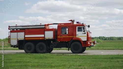 A fire truck is driving on the road towards the runway at the airport. Shooting from the side