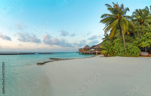 Amazing wide panorama of tropical Maldives island. Exotic beach background with blue lagoon  turquoise water and palm trees during beautiful sunrise. 