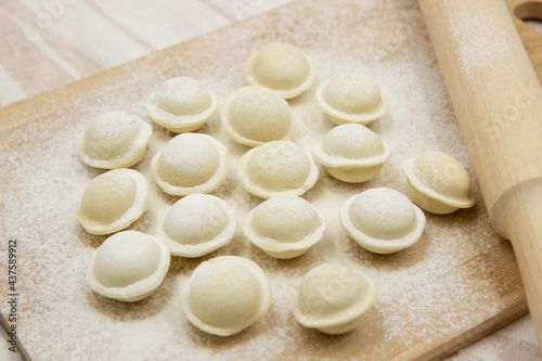 Raw Russian dumplings on a wooden board with a rolling pin.