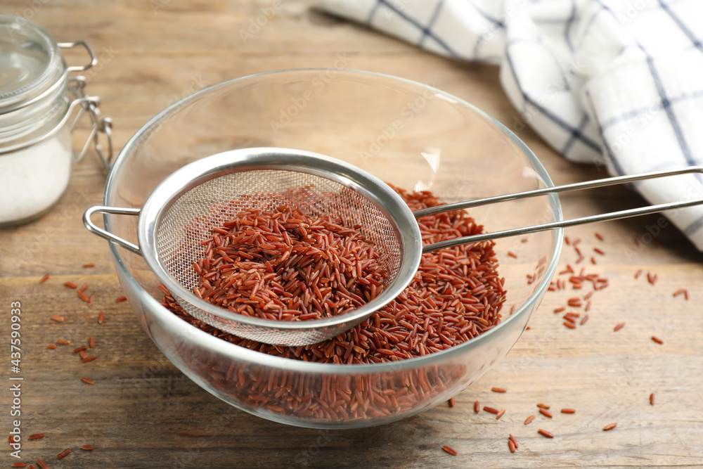 Sieve with brown rice in bowl on wooden table Sieve with brown rice in bowl on wooden table