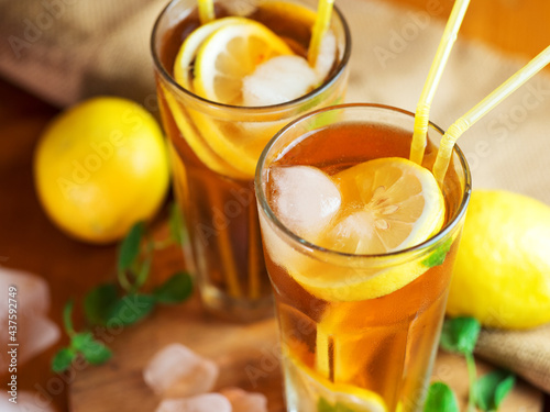 Two glasses of cold summer tea with lemon and mint on the wooden table. Refreshing ice drink