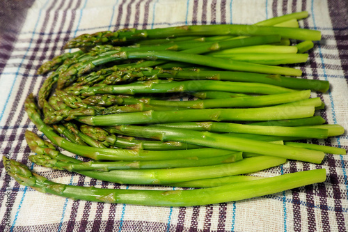 many pods of cooked green asparagus lie on white with a lilac towel. freshly brewed double dries from water. side view