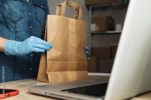 Courier preparing parcel package for delivery wearing protective gloves inside warehouse office - Main focus on hands