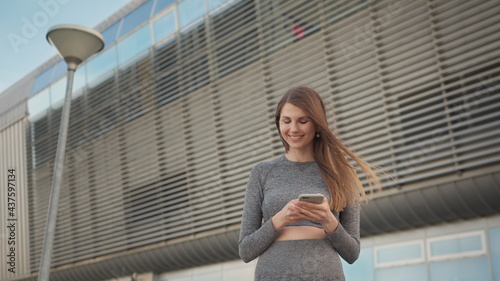 Portrait woman looking at smartphone while running outdoor. Close-up Of A Young Beautiful Sports Fitness Girl Holding A Smartphone In The Hands, Using A Fitness App. Modern City Shooting On the Street